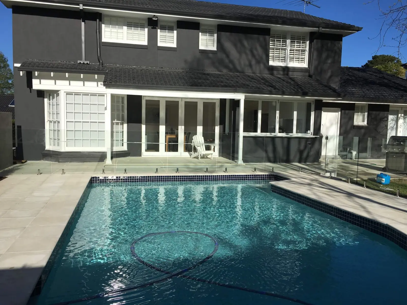 Pool in front of a dark two storey home with pale paving