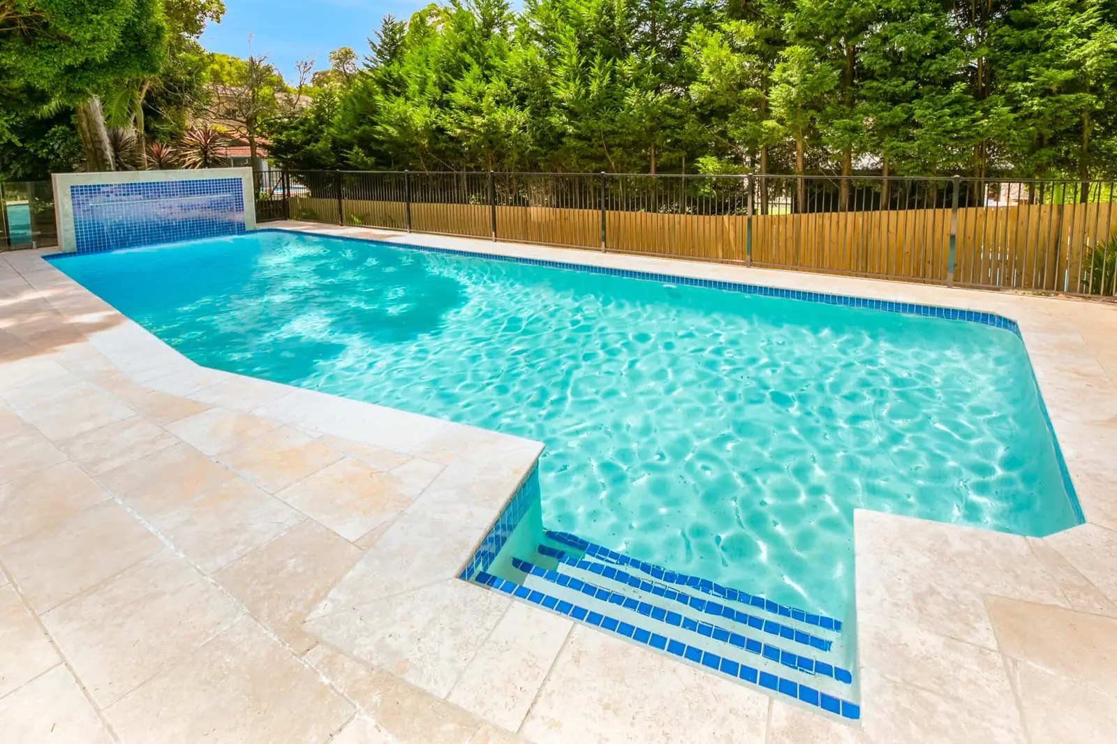 Bright blue pool with tiled entry steps and travertine surrounds