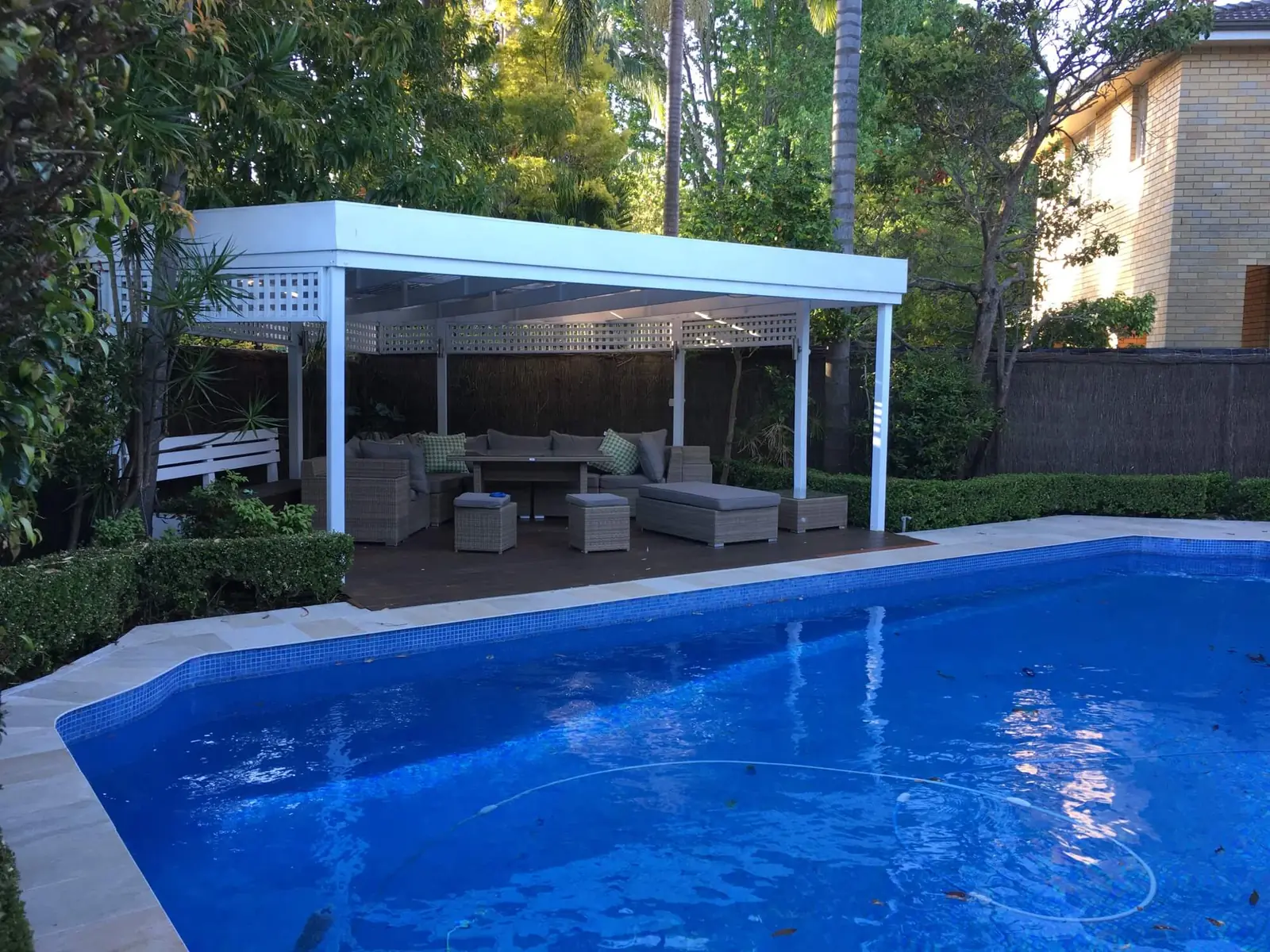 Deep blue pool beside a white pergola outdoor room