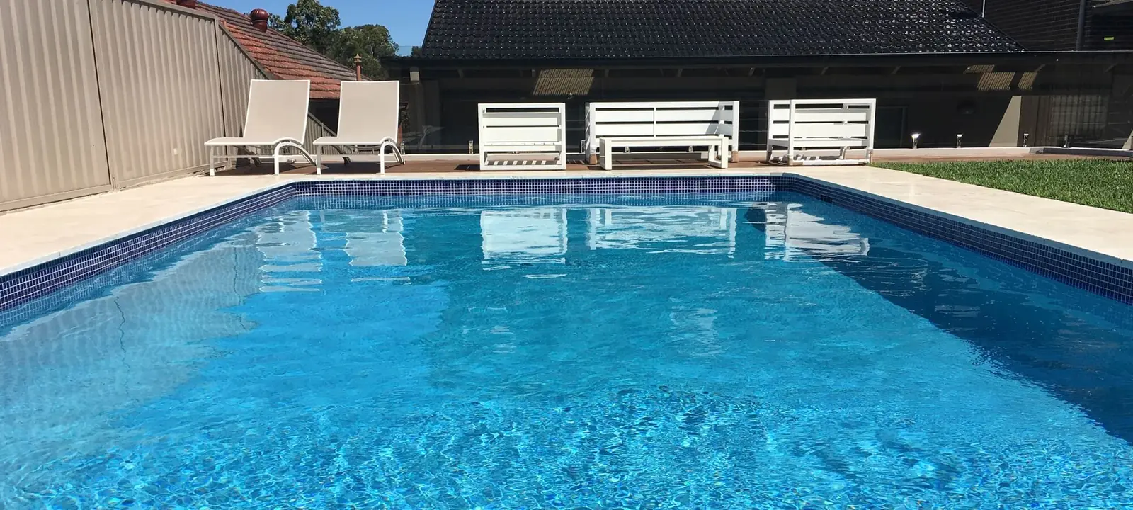 Renovated pool with clear blue water, tiled waterline and white outdoor seating