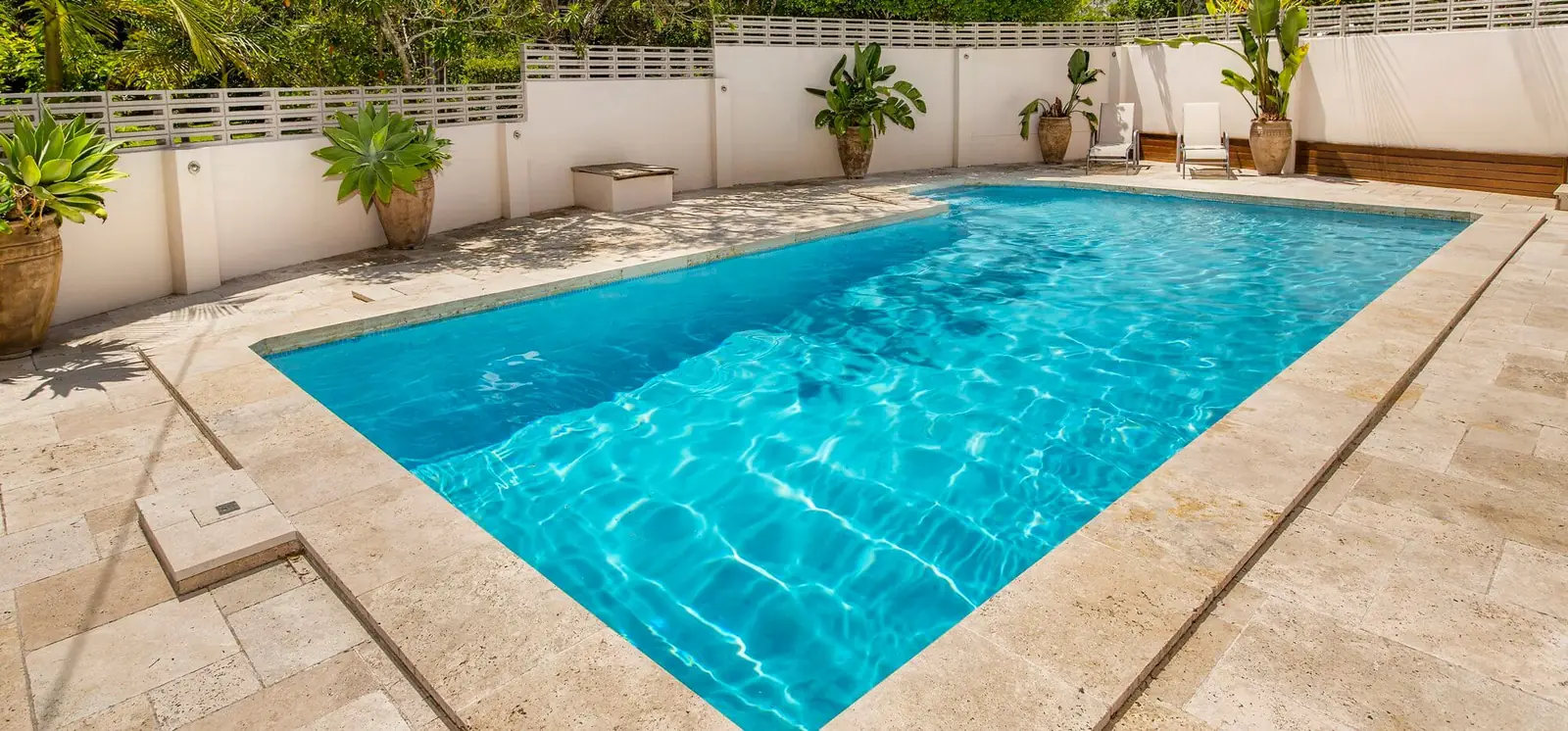 Rectangular pool with travertine paving surrounded by tropical plants